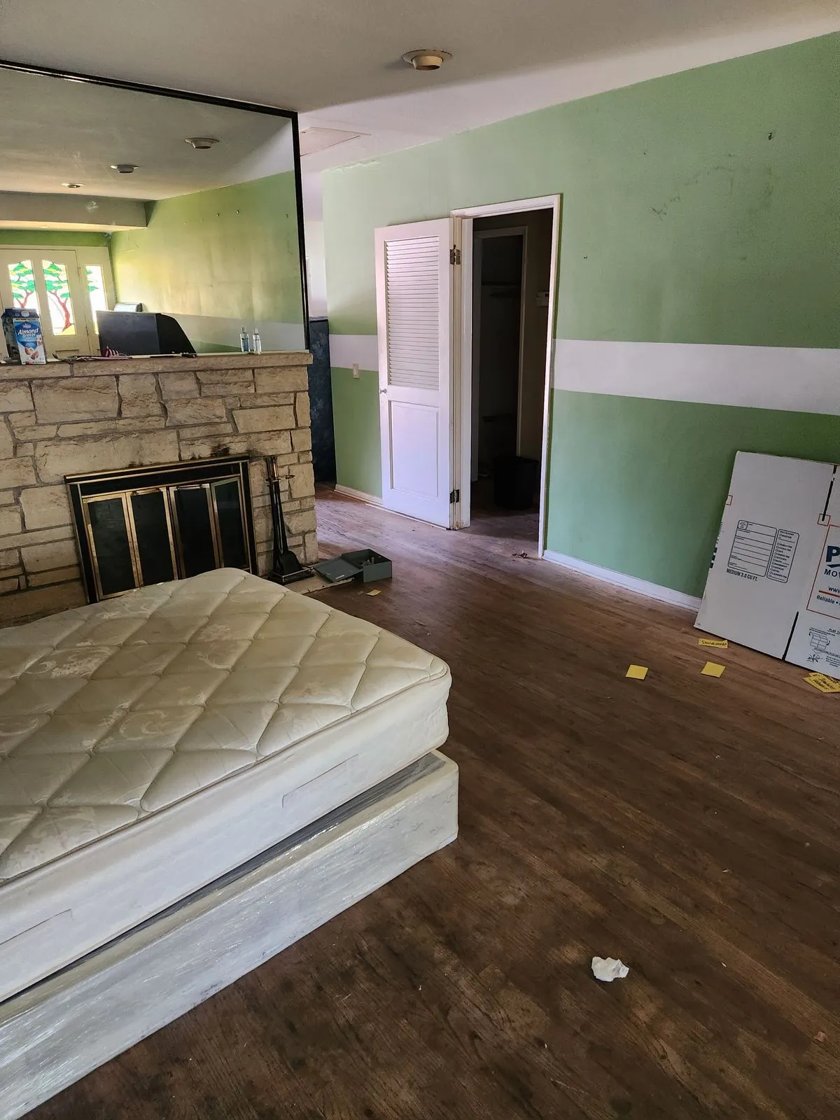 Dated living room with old stone fireplace, green walls, and worn flooring