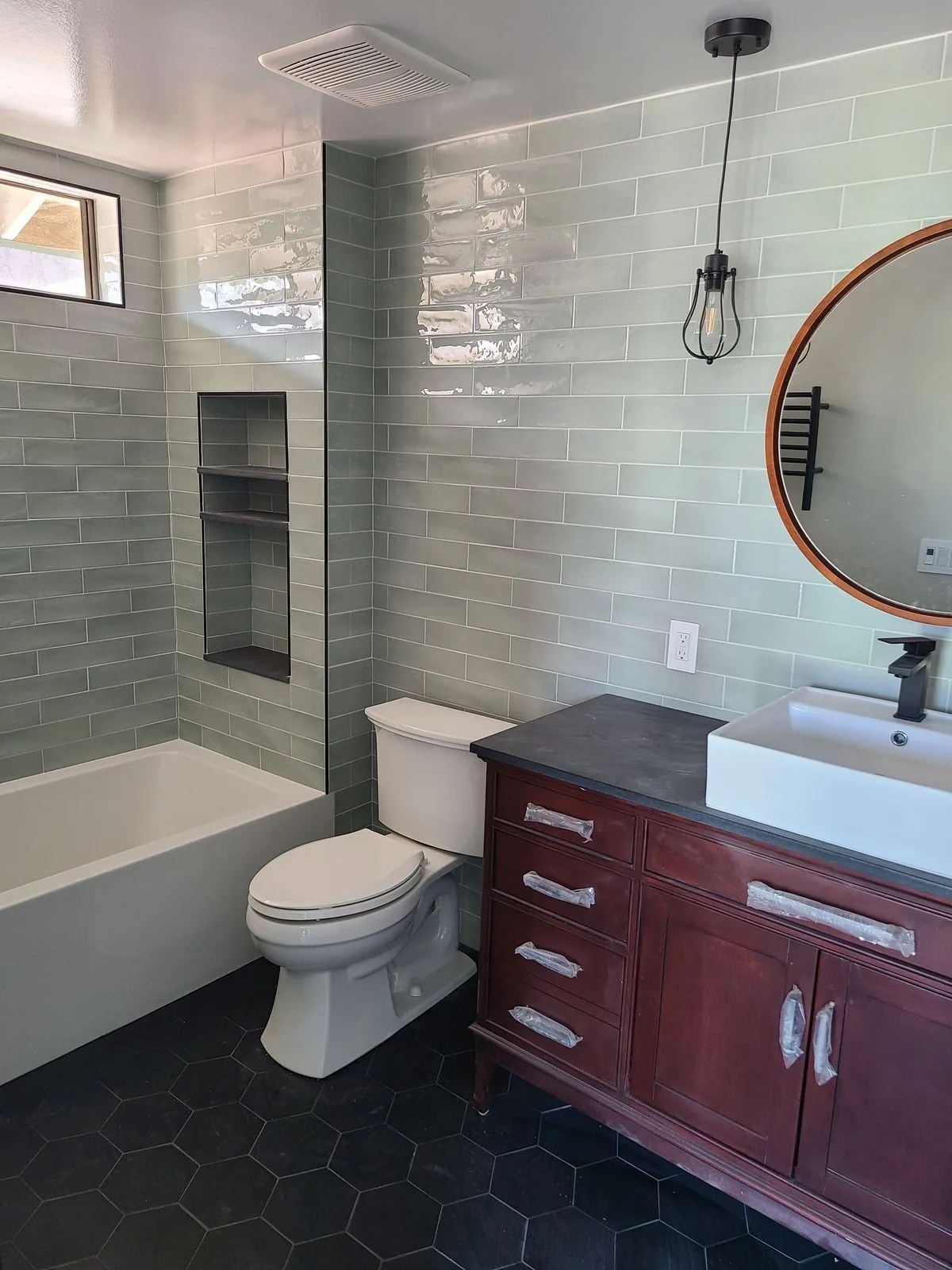 Renovated master bathroom with tile shower, dark hex flooring, and cherry vanity