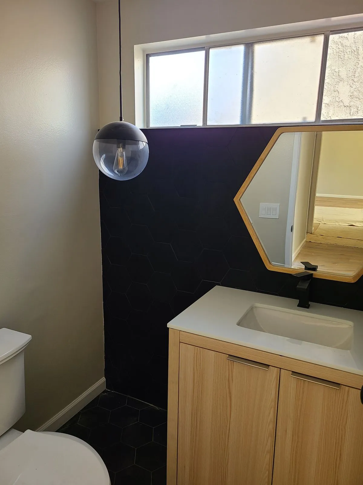 Modern powder room with dark hex tile wall, oak vanity, and globe pendant light