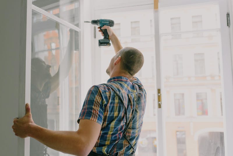 Professional handyman installing a window frame with a drill