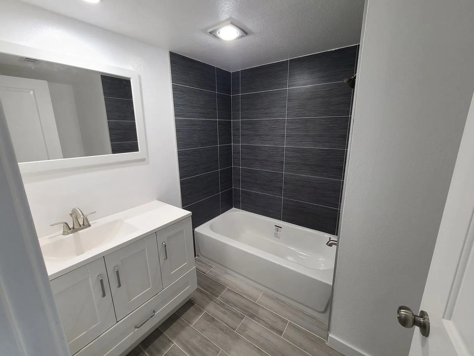 Full bathroom renovation with dark tile, white vanity and mirror